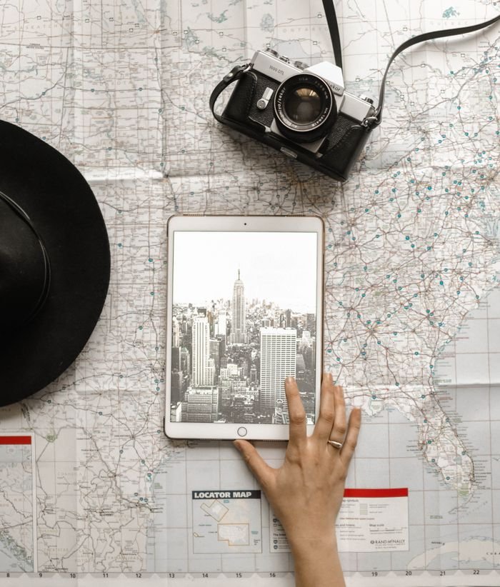 about-02 Flat lay of vintage camera, iPad with New York City skyline, and a hand on a map.