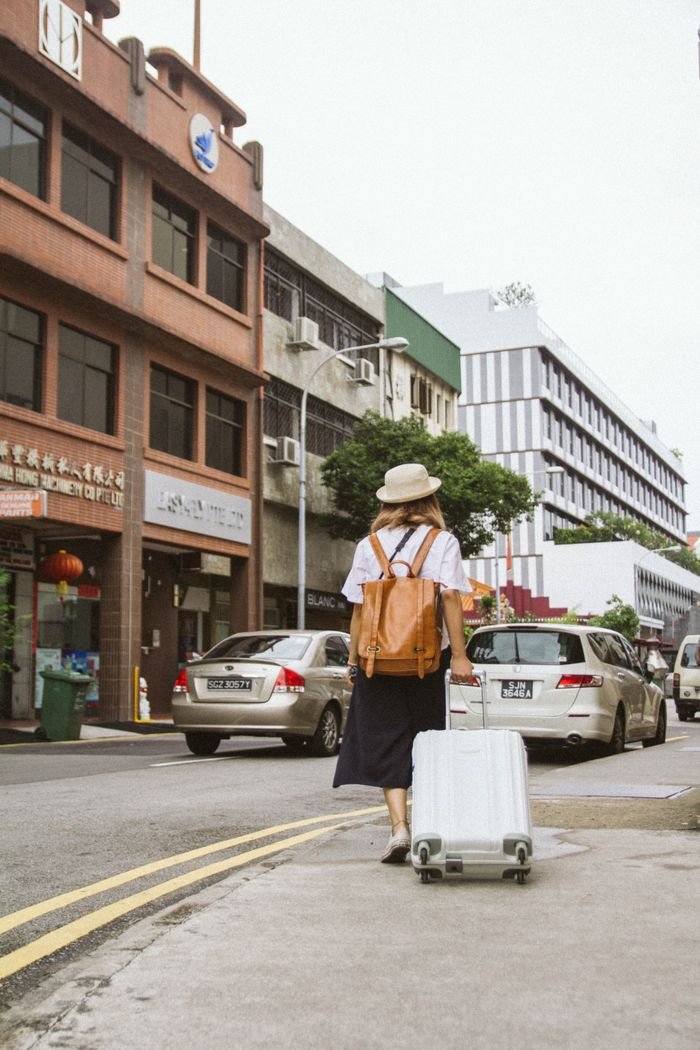 services-img A woman with a suitcase and backpack walks down a busy city street on a sunny day.