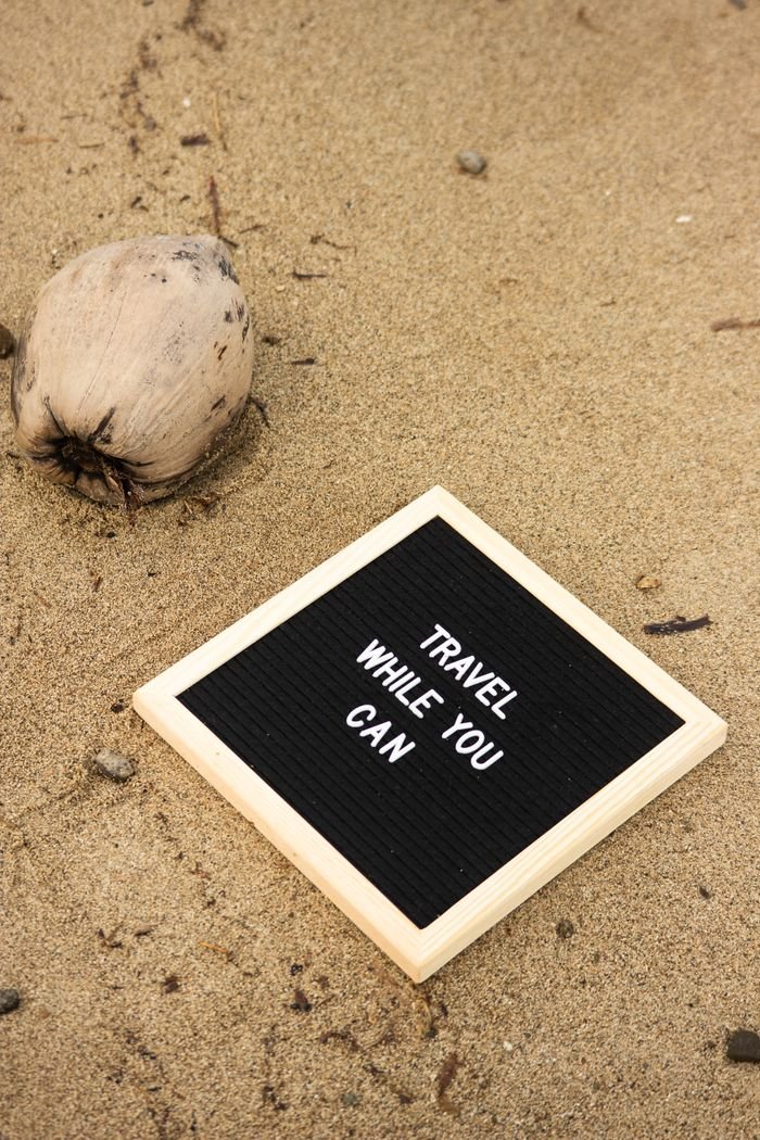 about-img Inspirational travel message on a letter board placed on sandy beach with a coconut nearby.